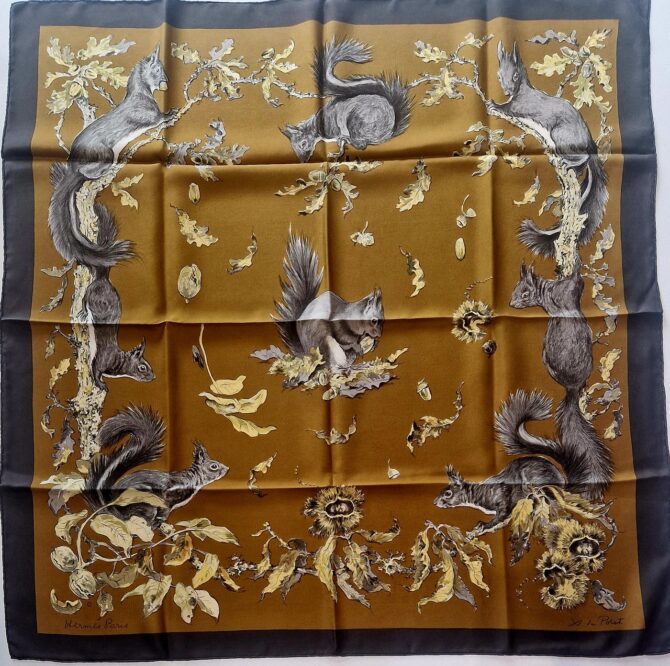 Carré Hermès en soie intitulé "Les Écureuils" de Xavier de Poret, édition de 1966, représentant des écureuils gris dessinés avec réalisme parmi des feuilles de chêne et des noisettes sur fond brun doré, bordé de noir.