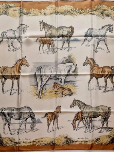 Carré Hermès en soie intitulé "Les Poulains" de Xavier de Poret, première édition 1960, illustrant des juments et poulains dans des scènes pastorales sur fond crème, encadré de bottes de foin dorées.