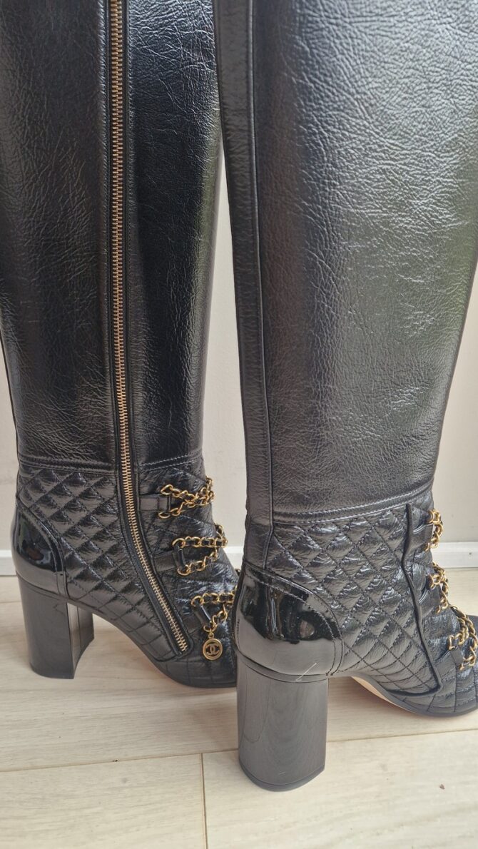Bottes Chanel en cuir noir matelassé avec chaînes dorées et logo CC – Chanel black quilted leather boots with gold chains and CC charm.
