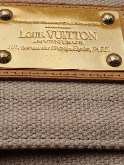 Détail de la plaque Inventeur dorée du sac Louis Vuitton Antigua Besace PM EN : Close-up of the gold Inventeur plaque on Louis Vuitton Antigua Besace PM