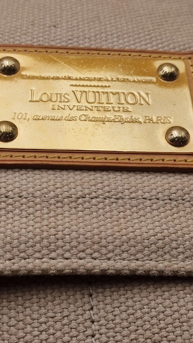 Détail de la plaque Inventeur dorée du sac Louis Vuitton Antigua Besace PM EN : Close-up of the gold Inventeur plaque on Louis Vuitton Antigua Besace PM