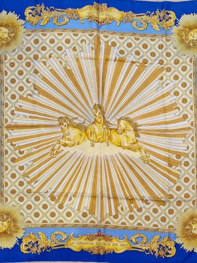 Foulard en soie bleu et or « La Grande Écurie du Roy – Versailles » signé Jacques Portier, représentant trois chevaux solaires entourés de motifs baroques et de visages rayonnants