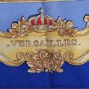 Foulard en soie bleu et or « La Grande Écurie du Roy – Versailles » signé Jacques Portier, représentant trois chevaux solaires entourés de motifs baroques et de visages rayonnants.