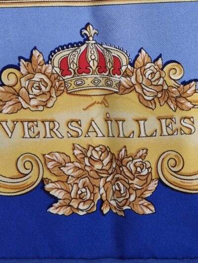 Foulard en soie bleu et or « La Grande Écurie du Roy – Versailles » signé Jacques Portier, représentant trois chevaux solaires entourés de motifs baroques et de visages rayonnants.